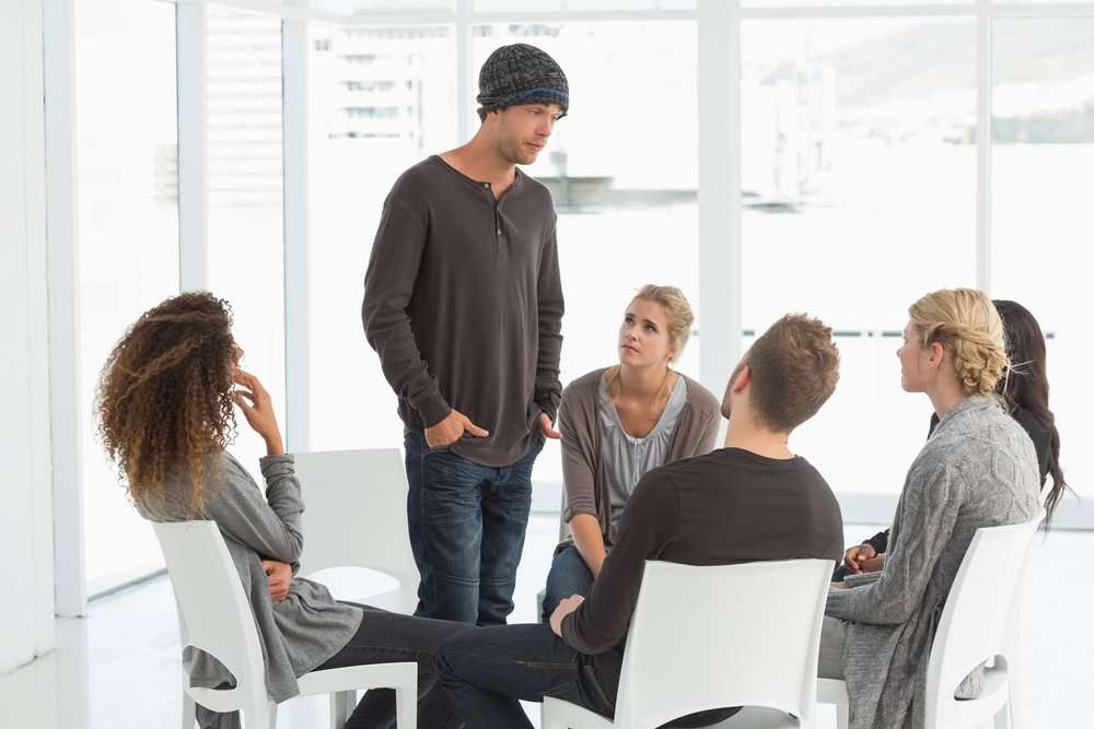 Rehab group listening to man standing up introducing himself at therapy session